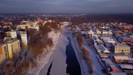 Wide-aerial-drone-view-over-the-city-of-Valmiera,-Latvia-and-frozen-river-Gauja-with-bridge