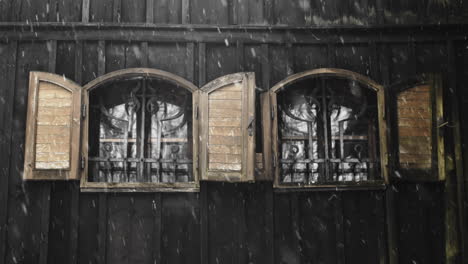 Snow-falls-outside-twin-iron-windows-on-dark-wood-panel-church-in-Cesky-Jiretin