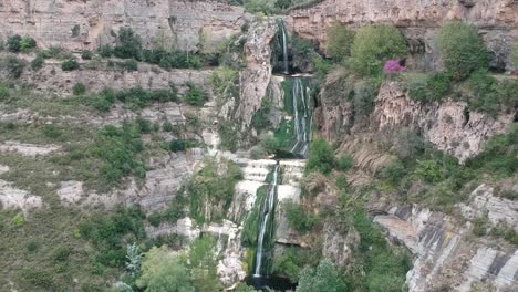 Aerial-views-of-a-waterfall-with-a-cave-and-an-old-building-in-Catalonia,-Spain