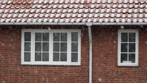 Snowflakes-are-falling-against-red-brick-house,-winter-day