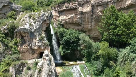 Luftaufnahmen-Eines-Wasserfalls-Mit-Einer-Höhle-Und-Einem-Alten-Gebäude-In-Katalonien,-Spanien