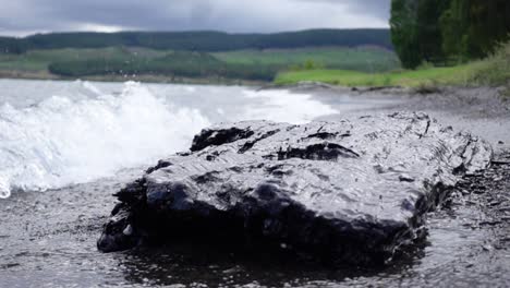 Wave-splashes-on-large-dark-rock-on-shore-of-Lake-Taupo,-slow-motion
