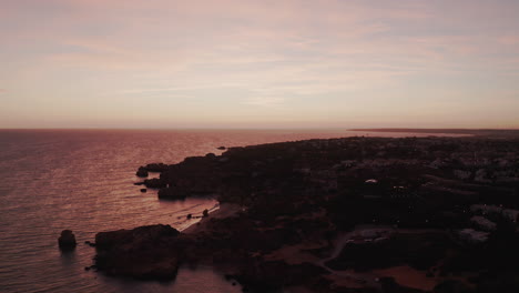 Aerial-view-showing-silhouette-of-coastline-and-red-colored-ocean-surface-during-sunset