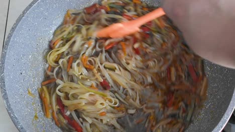 Man's-hand-stirring-noodles-and-chopped-vegetables-while-frying-in-a-wok