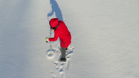 Girl-In-Red-Hooded-Jacket-Drill-Hole-On-Snowy-Ground-Using-An-Ice-Fishing-Auger---High-Angle-Shot