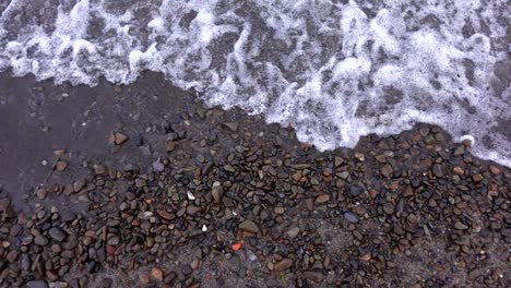 Above-natural-colored-rocks-on-beach-with-wave-rolling-in,-slow-motion