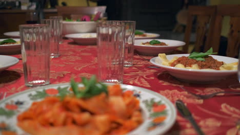 Zeitlupenkameraschwenk-Eines-Schön-Gedeckten-Tisches,-Pasta-Wird-Auf-Den-Tellern-Mit-Roter-Tischdecke-Serviert