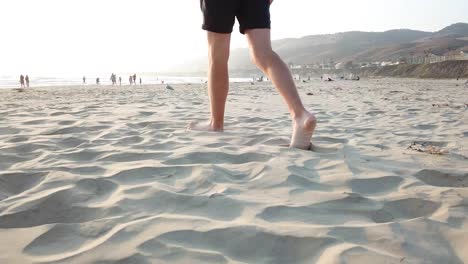 Untere-Hälfte-Eines-Mannes-Mit-Weißen-Füßen-Und-Gebräunten-Beinen,-Die-Am-Sandstrand-Entlang-Laufen
