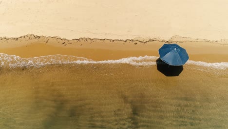 Aerial-top-down-drone-view-of-lonely-sun-umbrella-in-a-deserted-orange-sand-beach