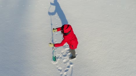 A-Woman-Struggles-As-She-Drilled-Hole-For-Fishing-On-Frozen-Lake-Using-Manual-Auger-During-Sunny-Winter-Day