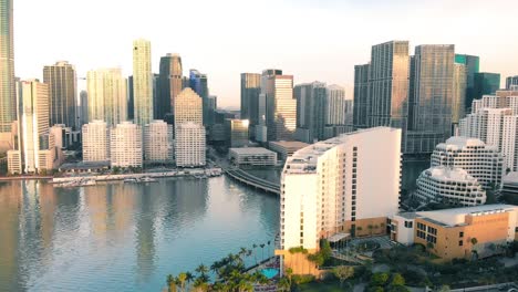 Aerial-view-of-Downtown-Miami-urban-city-center-south-of-the-Miami-River-Brickell-reflecting-in-the-water-at-sunrise,-slow-motion