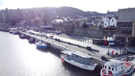 Idyllic-Conwy-castle-and-harbour-fishing-town-boats-on-coastal-waterfront-aerial-low-angle-dolly-right-reverse