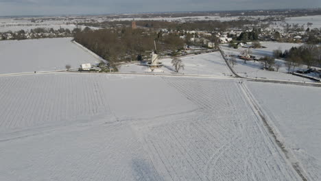 Aerial-overview-of-beautiful-snow-covered-rural-landscape-with-a-traditional-windmill-at-the-edge-of-small-town