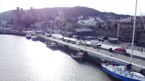 Idyllic-Conwy-castle-and-harbour-fishing-townscape-boats-on-coastal-waterfront-aerial-low-angle-reverse-right