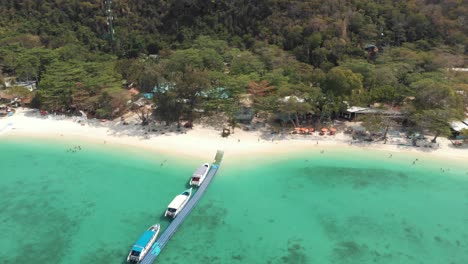 Banana-Beach-Pier-across-shallow-emerald-Sea-with-tourists-tour-boats-in-Koh-Hey-,-Thailand---Aerial-Tilt-down-Fly-over-rotation-shot