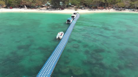 Floating-pier-with-moored-tourist-tour-boats-in-the-idyllic-emerald-water-of-Banana-Beach,-Koh-Hey-,-Thailand---Aerial-Low-angle-Orbit-shot