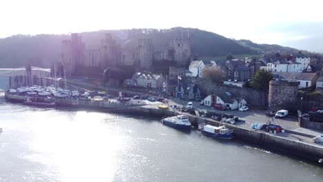 Idyllic-Conwy-castle-and-harbour-fishing-town-boats-on-coastal-waterfront-aerial-slow-push-in