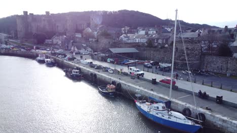 Picturesque-Conwy-castle-and-harbour-fishing-town-boats-on-coastal-waterfront-aerial-low-angle-dolly-forward-left