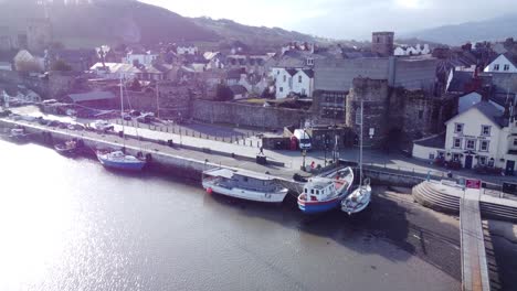 Idyllic-Conwy-harbour-fishing-town-boats-on-coastal-waterfront-aerial-push-in