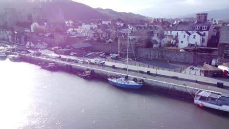 Idyllic-Conwy-castle-and-harbour-fishing-town-boats-on-coastal-waterfront-aerial-dolly-left-across-shimmering-water