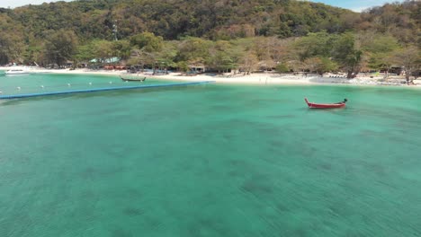 Idyllic-Banana-Beach-Bay-with-floating-dock-platform-and-rural-fishing-boats-moored-on-the-emerald-waters-in-Koh-Hey-,-Thailand---Aerial-ground-level-Fly-backwards-shot