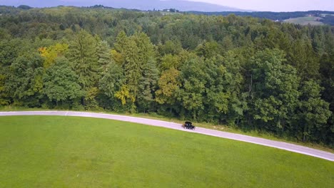 Scenic-aerial-view-at-old-timer-travelling-on-road-next-to-green-forest