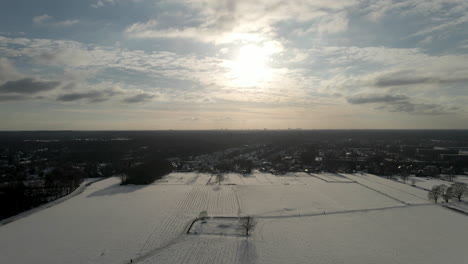 Aerial-of-snow-covered-meadows-against-a-setting-sun-with-a-small-town-in-the-background
