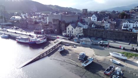 Picturesque-Conwy-castle-and-Welsh-harbour-fishing-town-boats-on-coastal-waterfront-aerial-dolly-left