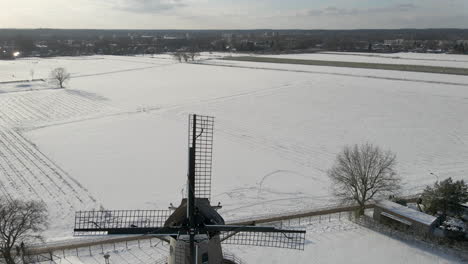aerial-of-snow-covered-rural-landscape,-revealing-a-traditional-dutch-windmill