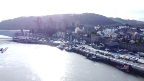 Idyllic-sunny-Conwy-castle-and-harbour-fishing-town-boats-on-coastal-waterfront-aerial-dolly-left