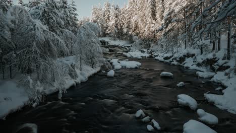 Zooming-out-time-lapse-of-forest-river-with-rocks-with-snow-cups-an-trees-covered-in-snow