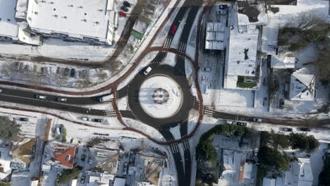 Top-down-aerial-of-traffic-using-roundabout-in-winter---drone-slowly-setting-down