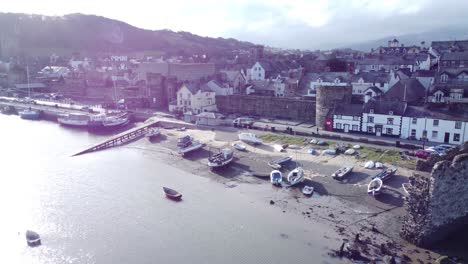 Idyllic-Conwy-castle-and-harbour-fishing-town-boats-on-coastal-waterfront-aerial-push-inland-slowly