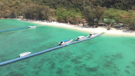 Schwimmender-Plattformpier,-Der-Von-Festgemachten-Ausflugsbooten-überfüllt-Ist,-über-Dem-Smaragdgrünen-Wasser-Des-Bananenstrandes,-Koh-Hey,-Thailand---Luftflug-In-Richtung-Absteigender-Schuss