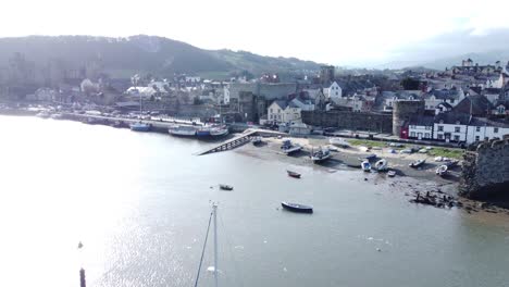Idyllic-Conwy-castle-and-harbour-fishing-town-coastal-waterfront-aerial-slow-rise-over-boats