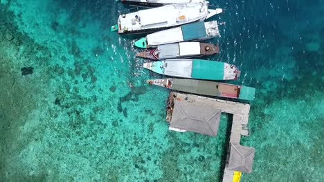 Circling-directly-above-tourist-boats-at-pier-on-exotic-Kanawa-Island,-Labuan-Bajo,-Indonesia