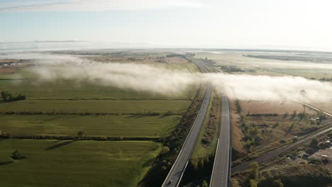 Patchy-dense-fog-over-interstate-highway-with-light-traffic-and-morning-sunlight