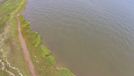 Drone-shot-over-bay-water-tracks-backward-to-shore-and-trees