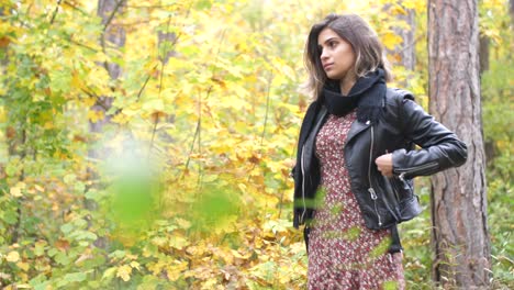 Wide-shot-of-Brunette-girl-in-autumn-forest,-stands-thoughtfully-and-looks-straight-and-puts-her-hands-in-the-pockets-of-her-jacket