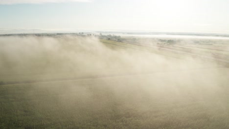 Pale-blue-sky-above-morning-fog-hanging-over-bright-green-farm-field-and-highway-passing-through-the-plains