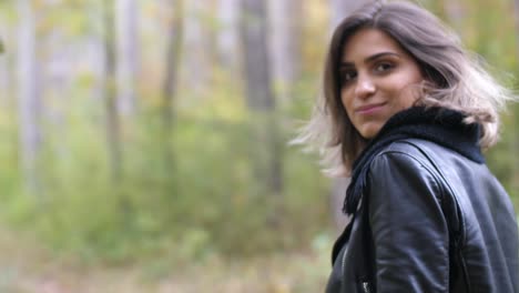 Close-shot-from-behind-of-Brunette-girl-in-autumn-forest,-walking-and-smiling-back-in-to-the-camera