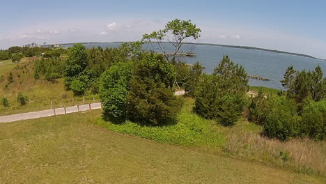 Drone-shot-rises-over-trees-to-reveal-bay-with-pier-and-breakwater-structure