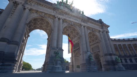 Upwards-angle-sideways-rotating-shot-of-the-Cinquantennaire-triumphal-arc-monument-in-Brussels,-Belgium,-on-warm-sunny-summer-day-with-blue-skies
