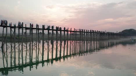 U-Bein-bridge-with-red-sunset-behind-revealing-traditional-boats-in-river