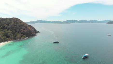 Idyllic-coastline-with-tourist-tour-boats-drifting-above-turquoise-shallow-sea-in-Koh-Hey-,-Thailand---Aerial-Ascending-Tilt-down-shot