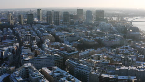 Wide-Panorama-aerial-shot-of-Bratislava-on-sunny-winter-morning-covered-in-snow,-high-rise-buildings-in-background