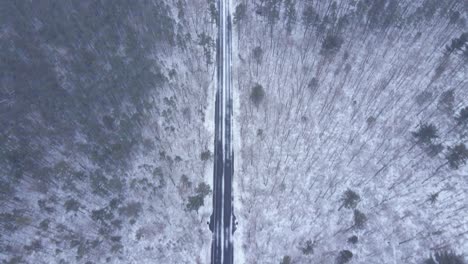 -Road-Between-Thick-Forest-Landscape-Covered-In-Snow-In-Winter---aerial-shot