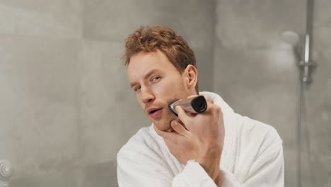 curly-handsome-guy-shaves-his-beard-with-a-clipper