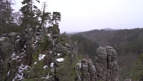 outlook-on-a-sandstone-rock-formation-in-Prachov-Rocks,-Bohemian-Paradise,-in-winter-with-Trosky-Castle-on-the-horizon,-truck-right