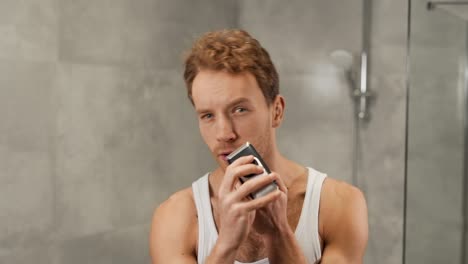 Handsome-sporty-man-in-t-shirt-shaves-with-electronic-razor-shaver